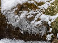 Kleine Eiszapfenenden an Eisgebilde über einem Fels am Bach